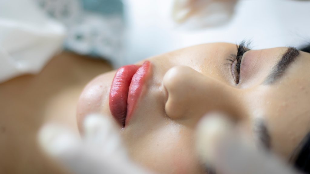 Close-up shot of a woman receiving a skincare treatment, highlighting red lipstick and eyelashes.